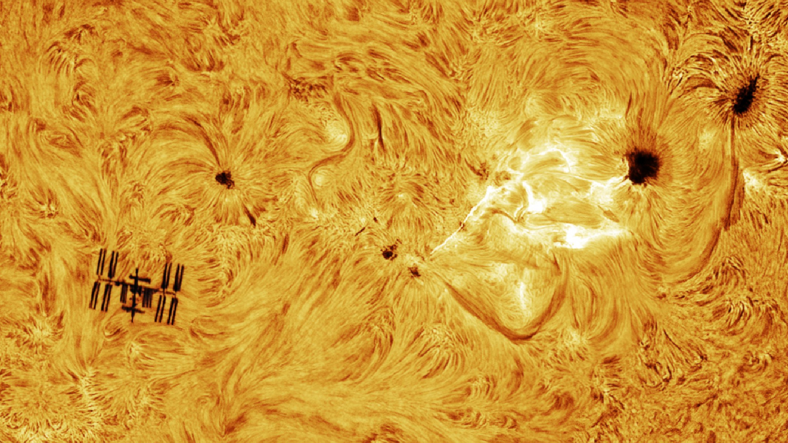 Close-up photo of the sun's surface showing the ISS next to bright loops of plasma from a flaring sunspot