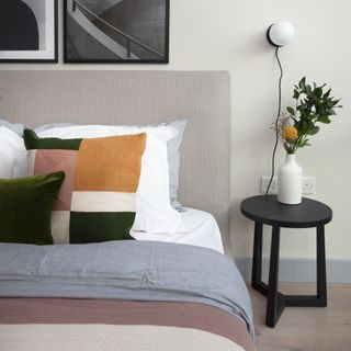 neutral bedroom with dressed bed with artwork and wall light and small bedside table