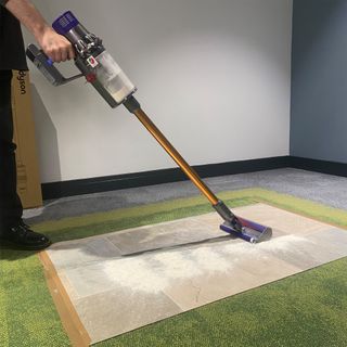 person vacuuming a green rug with a cordless Dyson vacuum