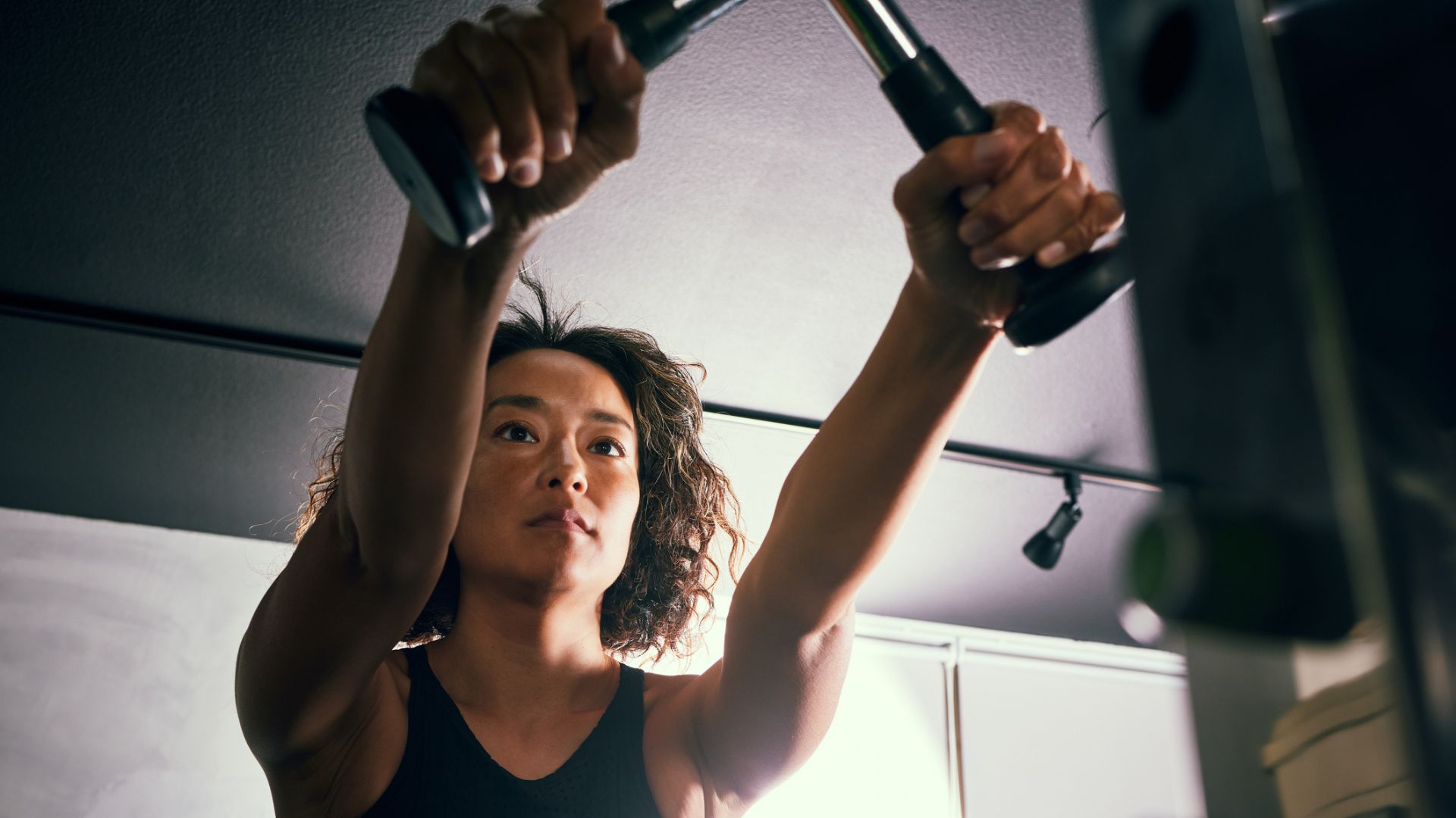 Close view of woman pulling handles of cable machine at the gym