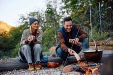 A couple in their late thirties or early forties cooking over a campfire.