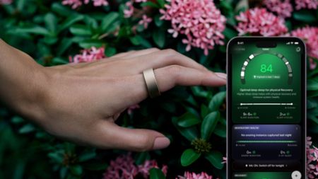 A woman's hand wearing gold Ultrahuman ring in front of greenery and pink flowers overlaid by iphone screen displaying Sleep Cycles data