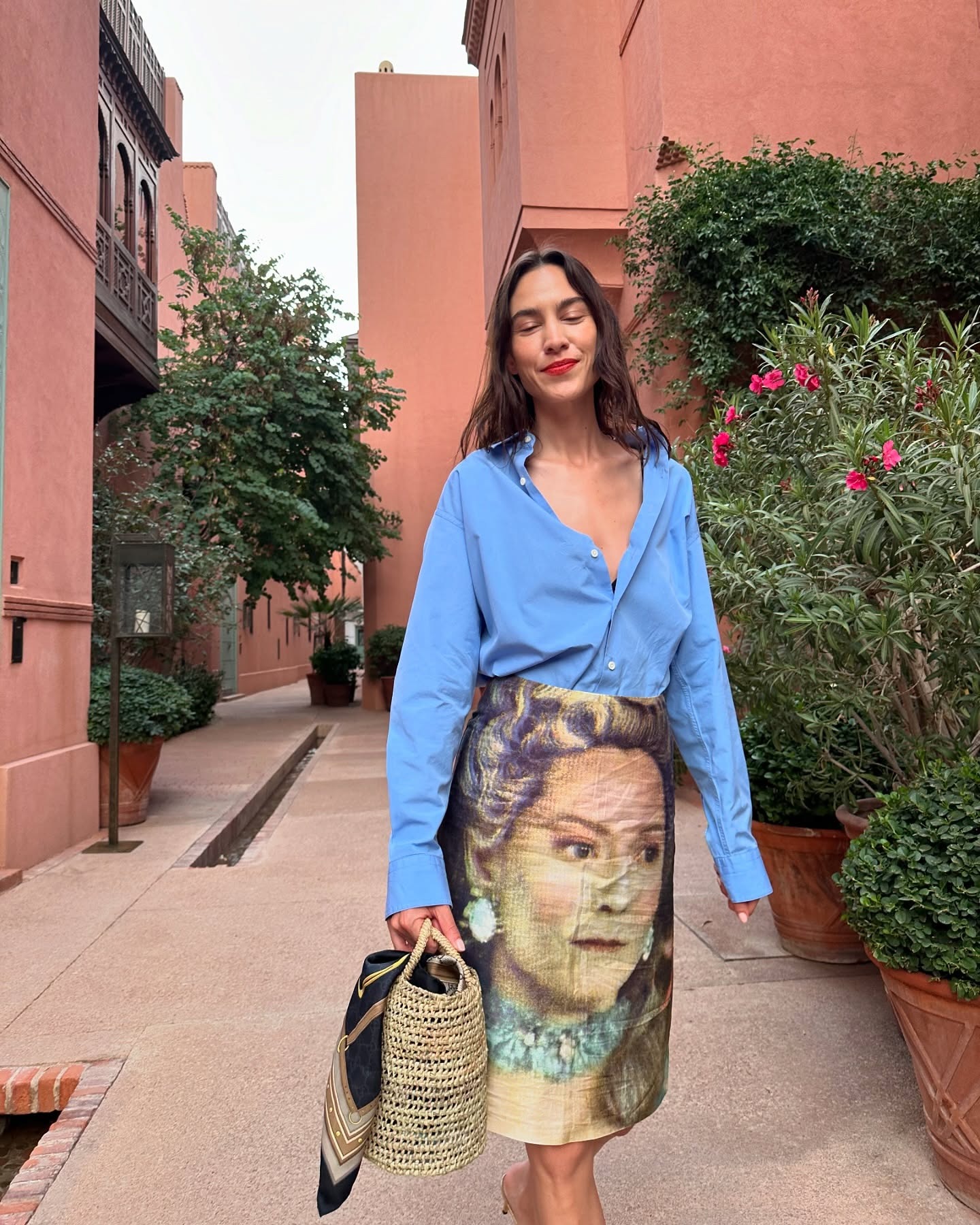 Alexa Chung wears a blue button-down shirt with a printed skirt and raffia bag in Marrakech.