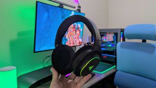 A Razer Barracuda X Chroma headset held in the hand with its RGB lighting enabled.