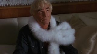 Burt Reynolds wearing a feather boa and looking up from a couch in Stripteaase