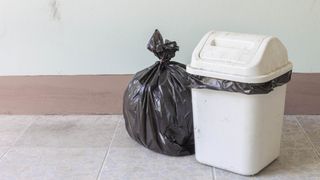 A kitchen trash can with a bag of trash next to it