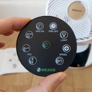 A close up of the black circular remote in front of the MeacoFan 1056 Air Circulator