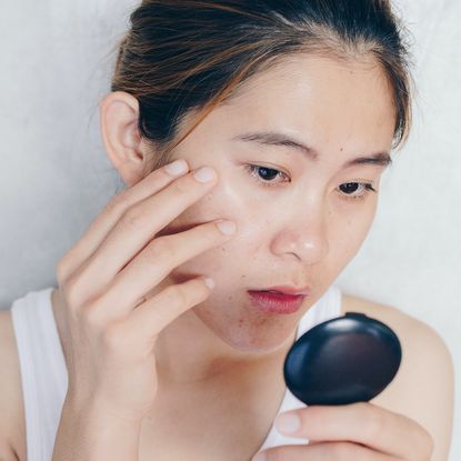 woman looking at acne in handheld mirror