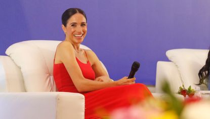 Meghan Markle wears a red dress with thin straps by Orire while onstage at a Women in Leadership panel