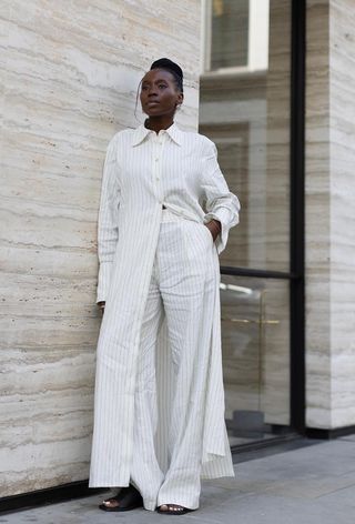 a woman's shirtdress outfit with a white pinstripe dress styled over trousers and black slides