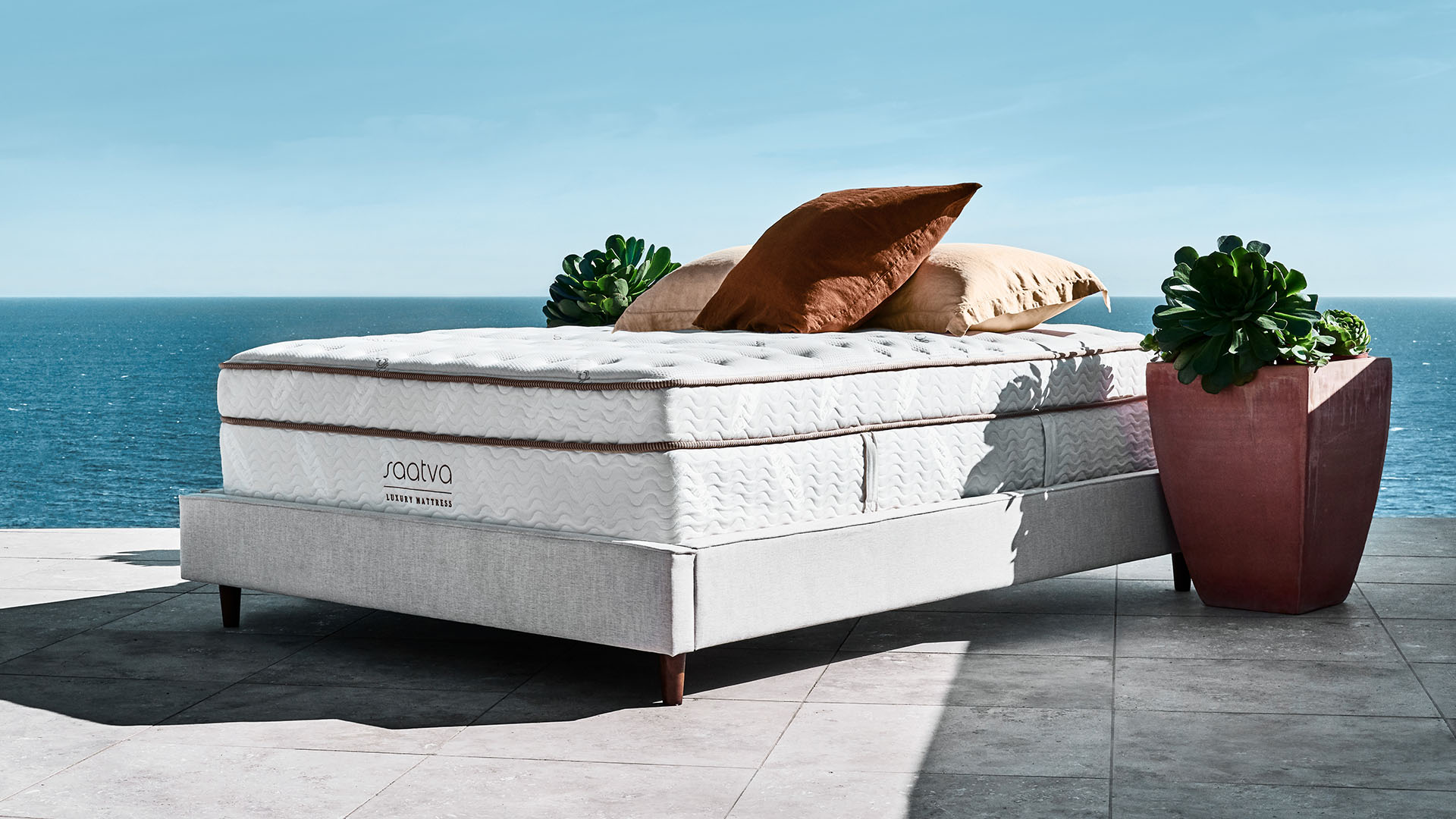 Saatva Classic mattress on a grey bed frame in an outdoor space overlooking a blue ocean