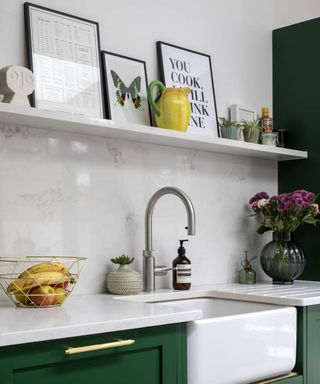 A modern kitchen with white butler's sink, round kitchen faucet, fruit bowl, flowers in vase and shelf with framed wall art decor