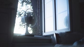 Top 10 tips for how to sleep when it’s hot at night: An image showing a fan placed near an open window to boost cooler airflow into the bedroom at night