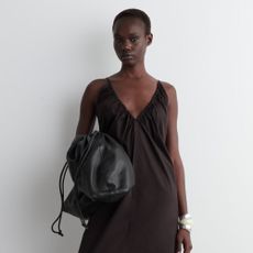 Woman wears brown ruched neck dress, carries black leather clutch bag, wears silver metal bracelets