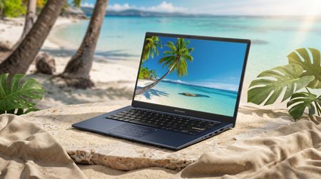 A sleek laptop sits on sandy beach with palm trees, ocean backdrop on screen. Sunlight shines, creating a serene and tropical vibe.