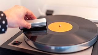How to clean vinyl records: a person uses an anti-static record brush to clean the surface of a vinyl record before playing it