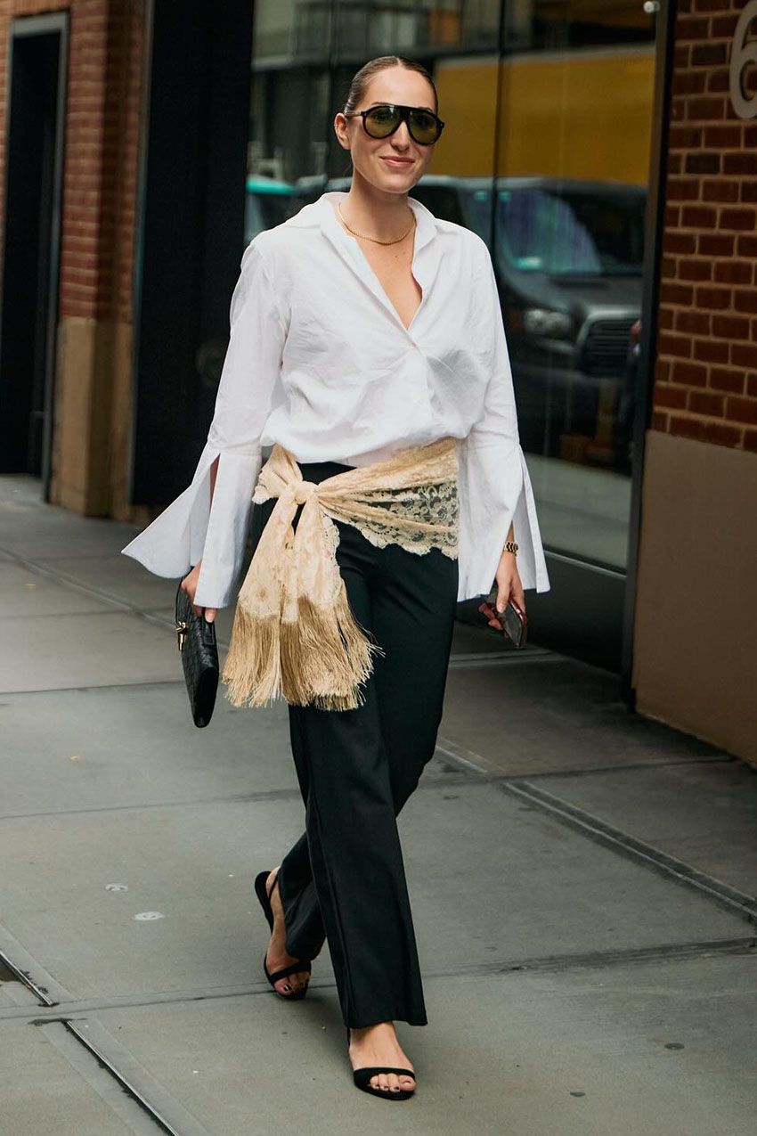 A woman wearing a white button down, black pants, black sandals, and black sunglasses