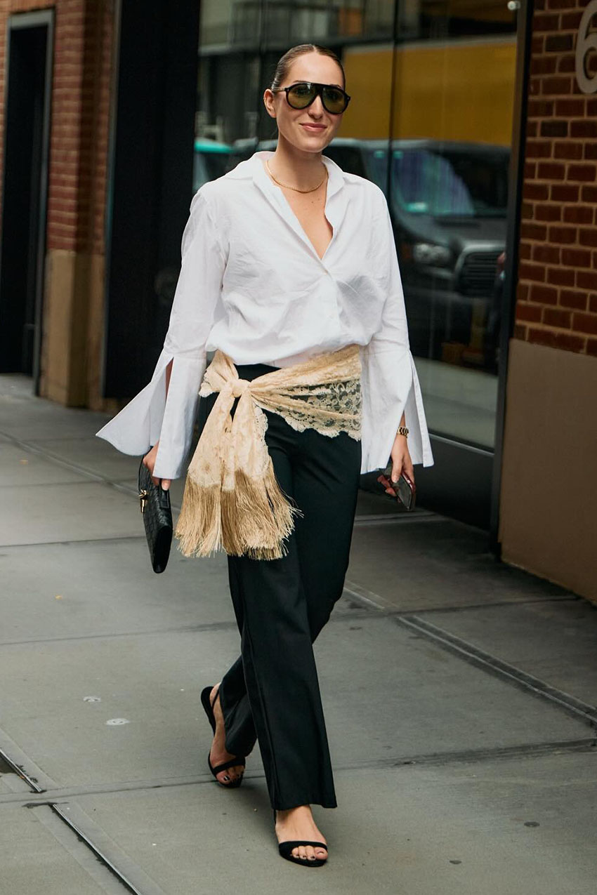 A woman wearing a white button down, black pants, black sandals, and black sunglasses