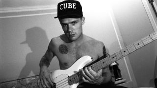 Musician Flea of the Red Hot Chili Peppers poses shirtless in his hotel room for a portrait, while holding his guitar and wearing a baseball cap which says "Cube" in August 1992 in New York City, New York.