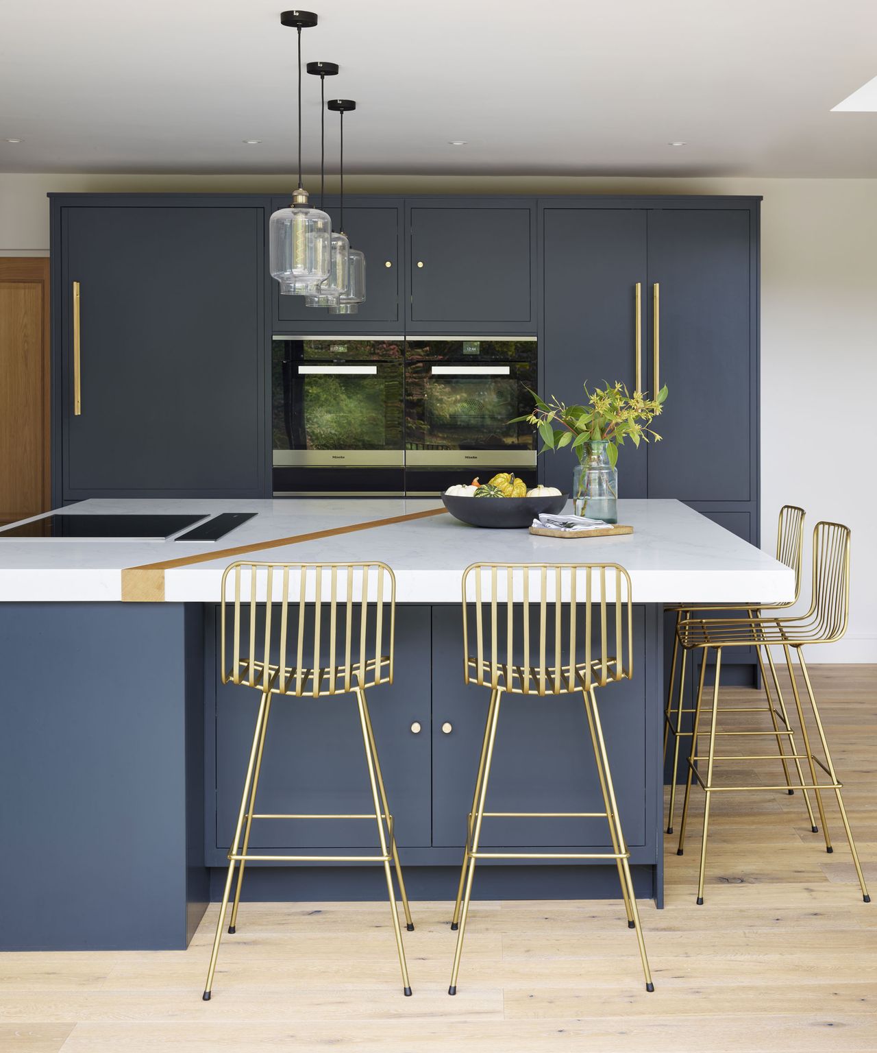 A neutral kitchen with blue cabinetry and gold metal bar stools showing how to choose kitchen island size.