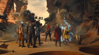 a group of people in bright clothing and armor stand in a sandy canyon on a desert planet