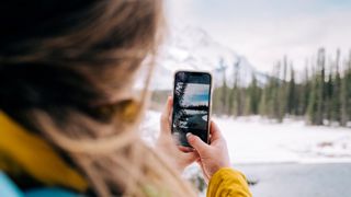 Over the shoulder perspective of a woman taking a photo with a smartphone in the Canadian Rocky Mountains