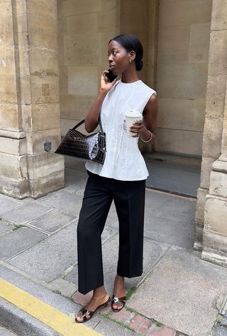 a photo showing what to wear to the office in the summer with a woman wearing a white pleated sleeveless blouse with black trousers and brown mules and a brown crocodile bag