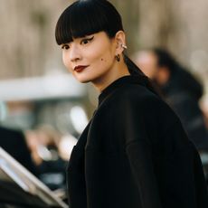 attendee at paris fashion week fall 2024 with blunt bangs, winged eyeliner, and dark lipstick