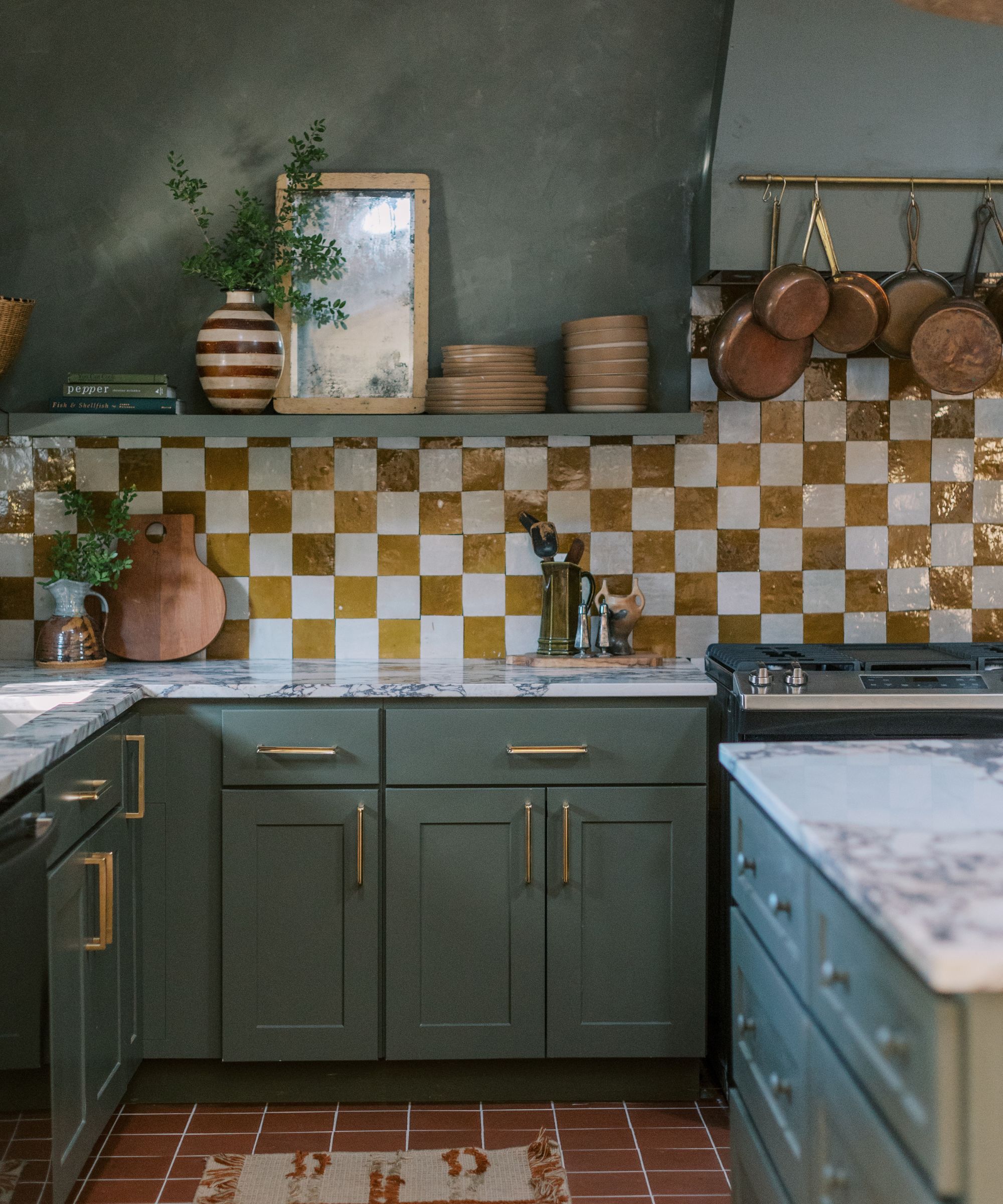 a kitchen with green cabinets and green limewashed walls, a white and tan checker printed backsplash, gold hardware, and white marble countertops