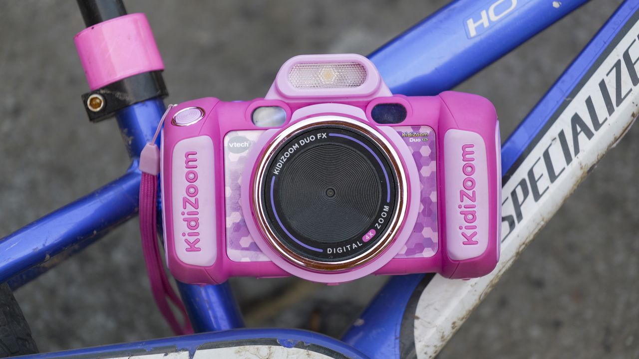A pink V-Tech KidiZoom Duo camera resting on the blue and white frame of a kid's bike