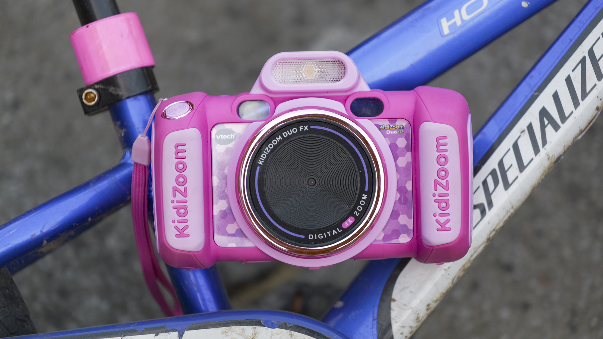 A pink V-Tech KidiZoom Duo camera resting on the blue and white frame of a kid's bike