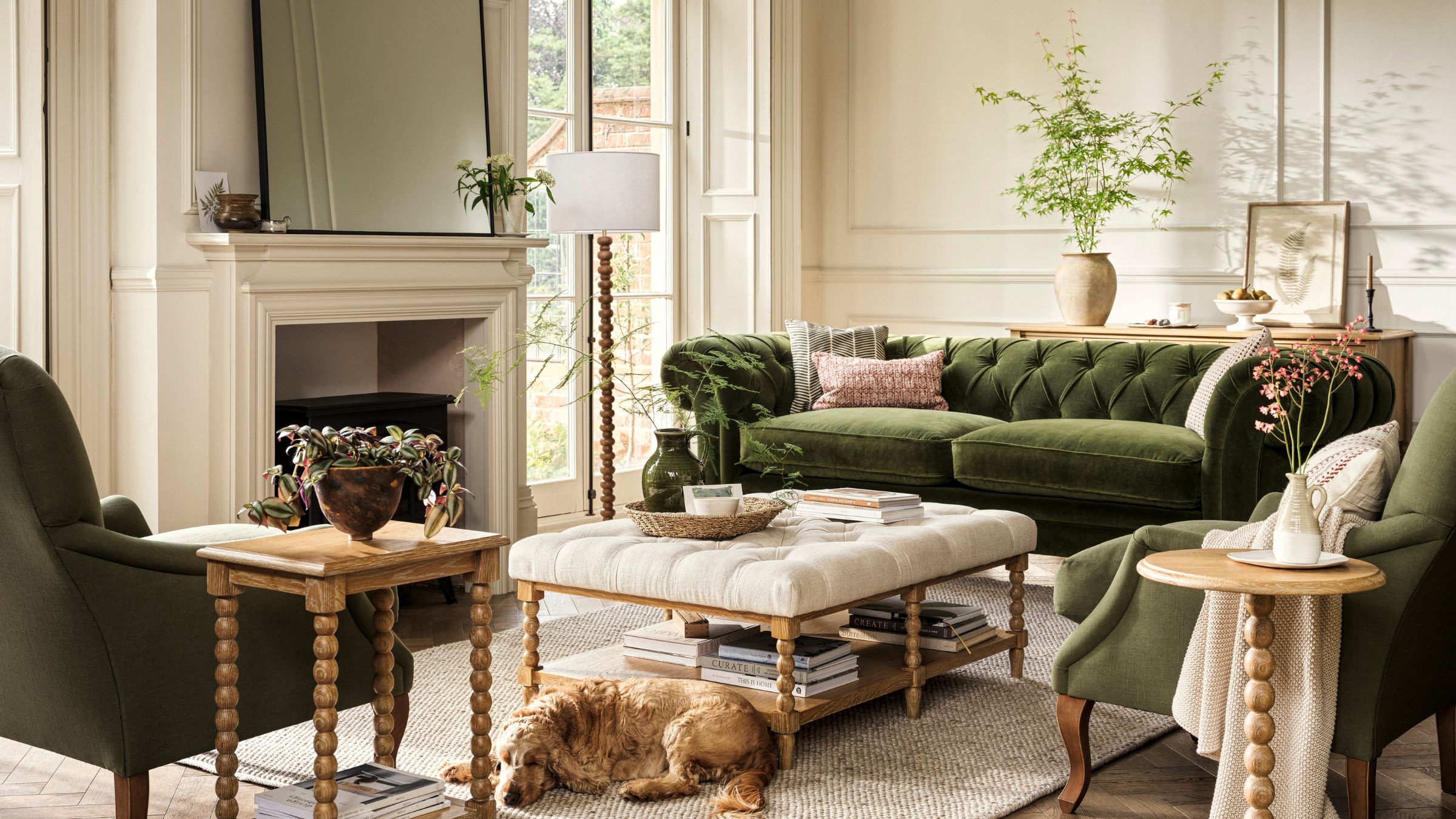 Cotswold Company x National Trust designed living room with solid oak bobbin furniture, green velvet upholstery and white walls, dog on the floor