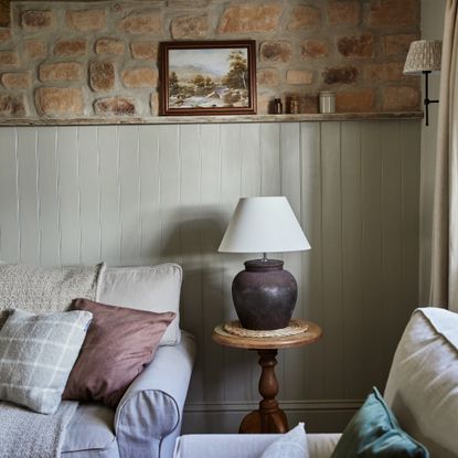 A neutral rustic living room with a half-panelled wall and the top half made with exposed stone