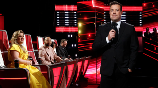 Carson Daly is pictured in front of The Voice coaches.