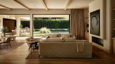 a neutral organic modern living room and open plan dining area with large fireplace and linen couches opening up to a pool deck and outdoor kitchen