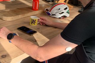 A Supersapiens glucose monitor in a man's arm at a kitchen table