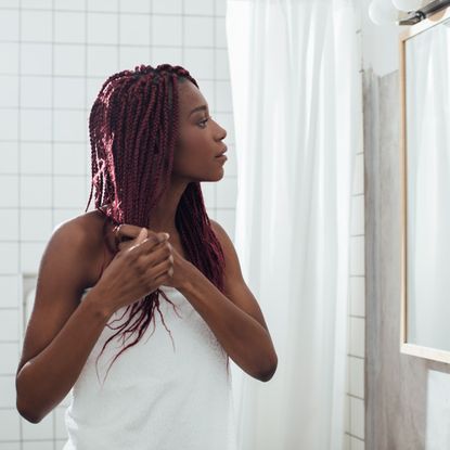 Young woman standing at bathroom and looking at mirror while holding hair.