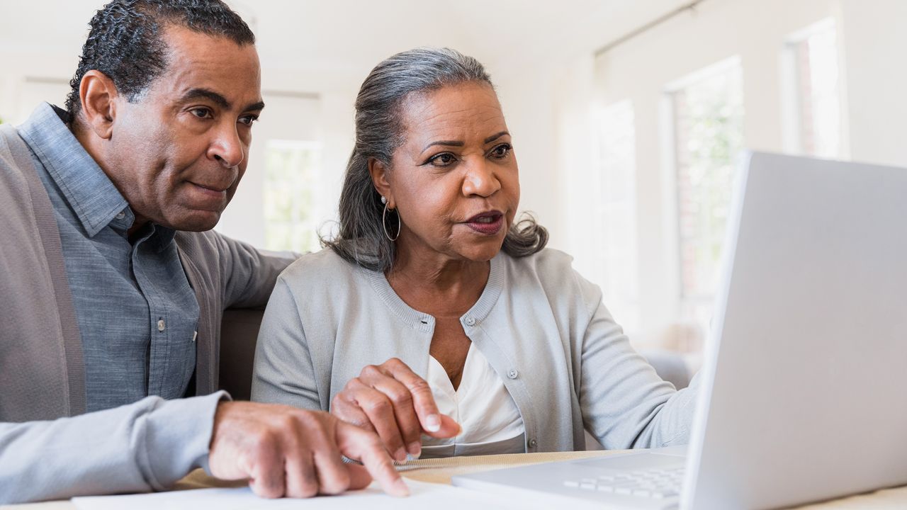 An older couple looks at a laptop and paperwork, looking like they&#039;re deciding what to do.