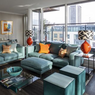 living room in apartment with teal sofa and pouffe and orange cushions and table lamps