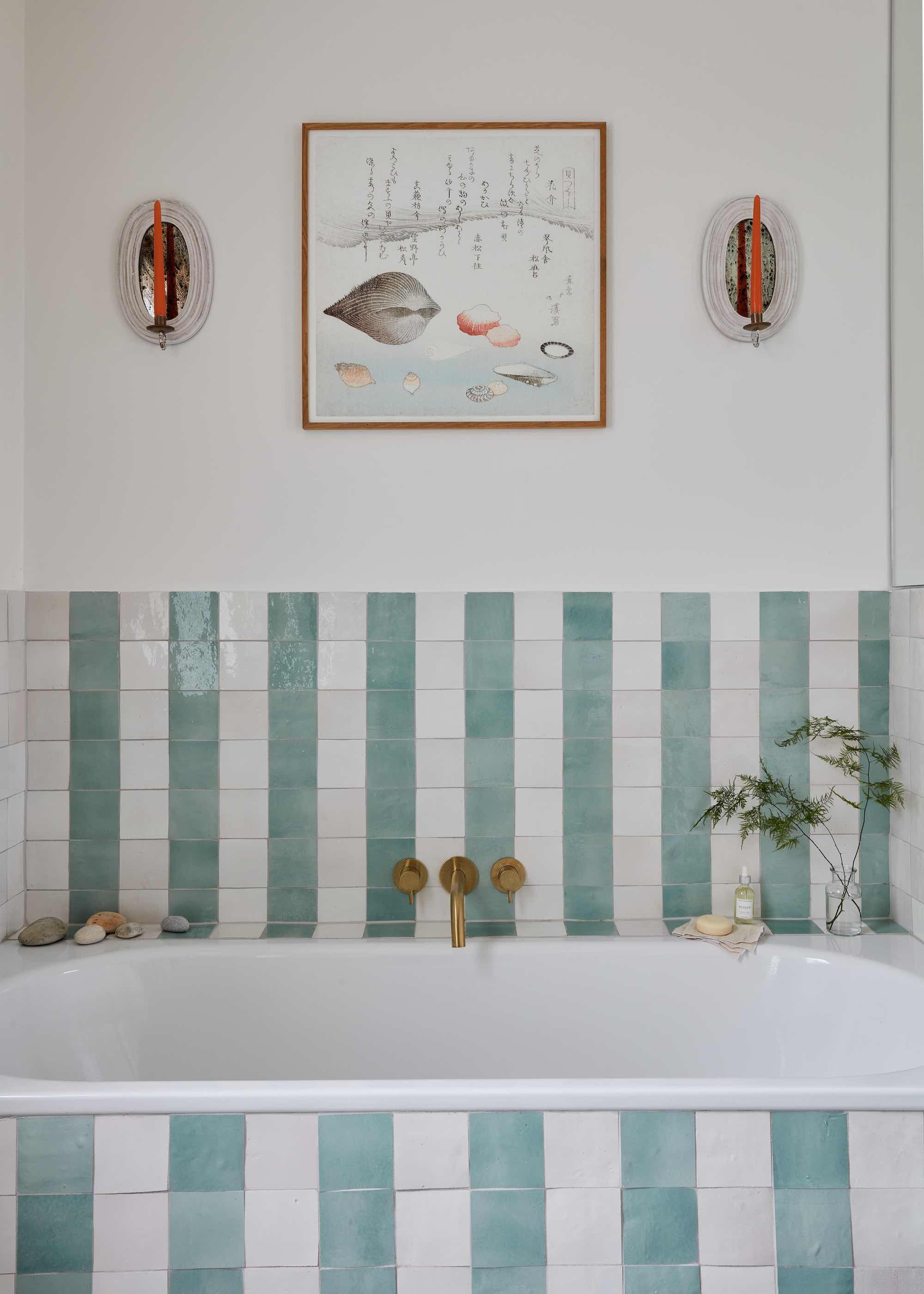A green and white striped bathtub with hanging artwork above in between two lights