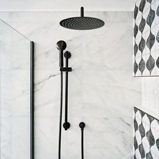 a black showerhead and handheld shower with a marble tiled wall beside a black and white patterned tile wall