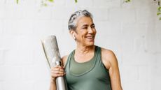 Mature smiling woman holding a water bottle and yoga mat