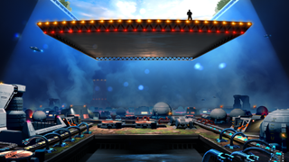 A man stands in a power pose on a platform being lowered into a dark space with assembly lines