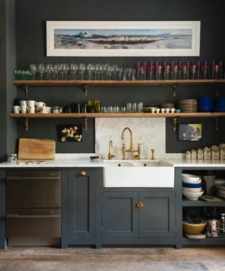 dark blue kitchen, open shelving with glassware, marble backsplash and countertop, white butler sink, wooden floorboards, deVOL