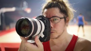 Photographer James Artaius holding the Canon EOS R1 in front of a basketball game