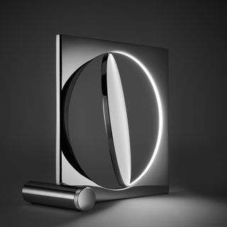 View of the chrome-plated 'Moonsetter' floor lamp that features a rotating metal disc that mimics the moon. It is pictured against a dark coloured background