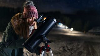 Young woman uses telescope to look at the night sky