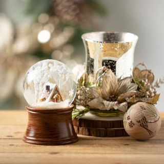 a Twillery Co Christmas Snow Globe next to a candle and bauble