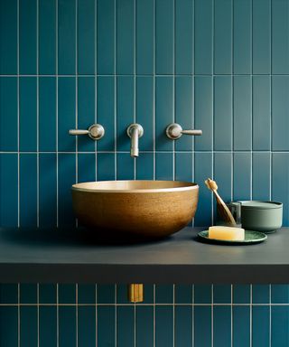 Teal subway-style tiles fixed in vertical behind a brushed brass sink