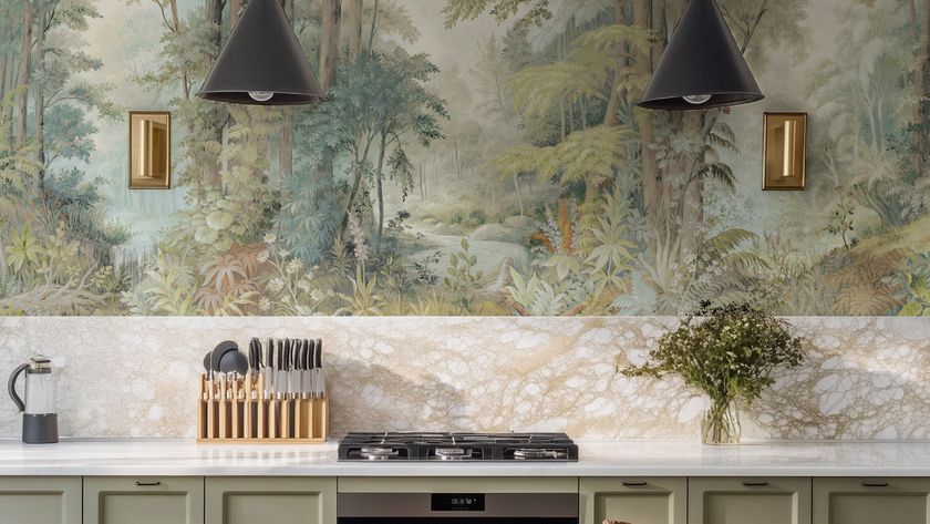 kitchen with sage green units, part marble effect tiled splashback, forest inspired wallpaper mural above, brass wall lights, black pendant lights, hob on worktop and kitchen accessories